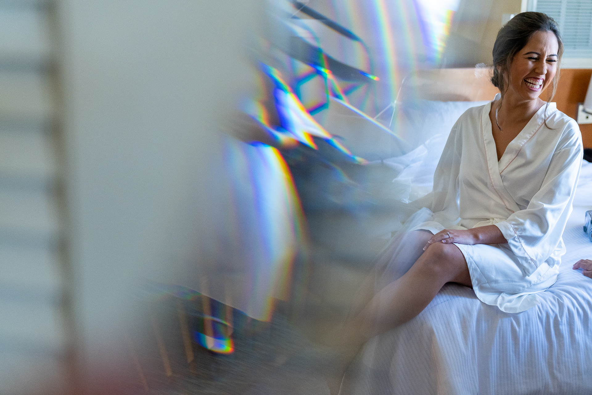 A woman in a white robe sitting on a bed, captured by wedding photographer Thomas Kim.