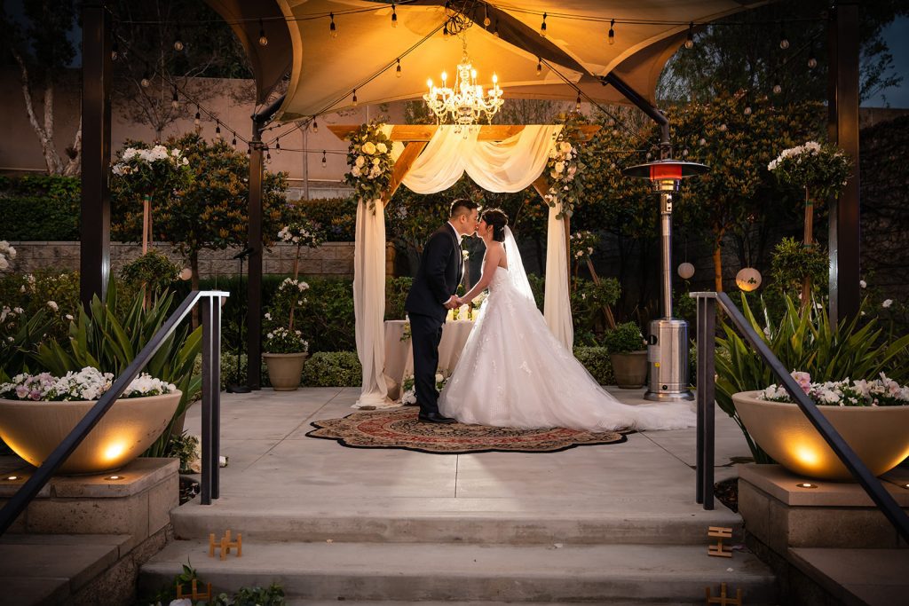 A bride and groom kiss in front of an outdoor wedding ceremony captured by photographer Thomas Kim.