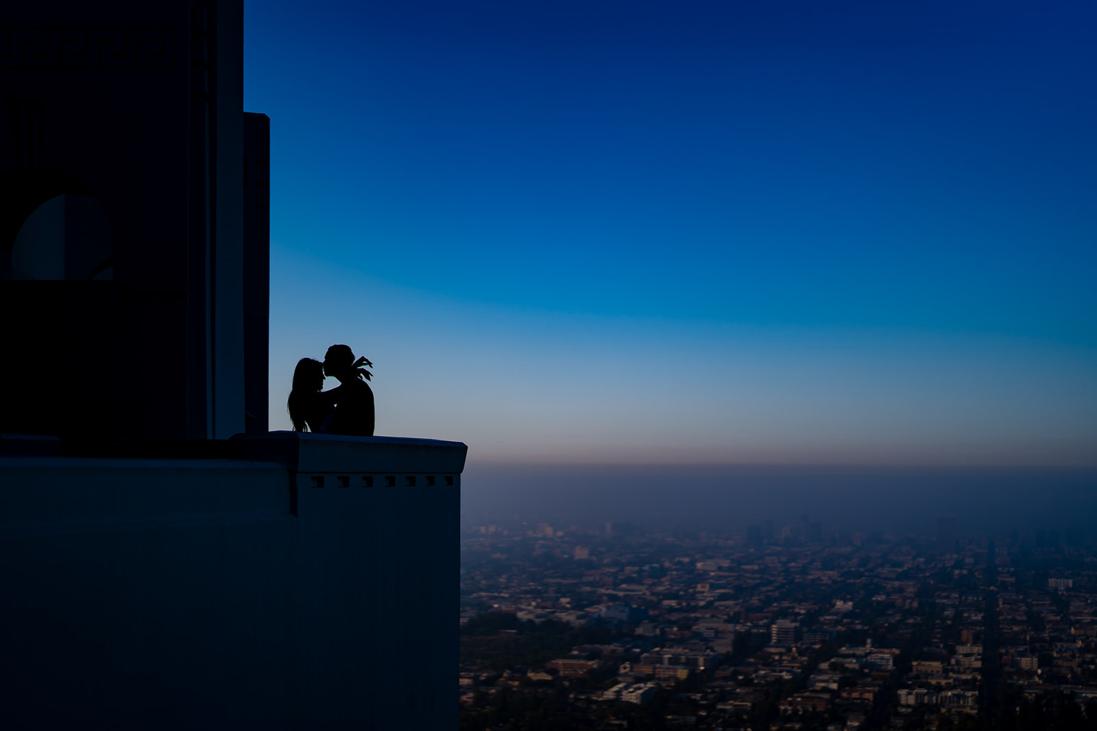ThomasKim_photography V & J Engagement Session featuring a couple sitting on a ledge overlooking a city.