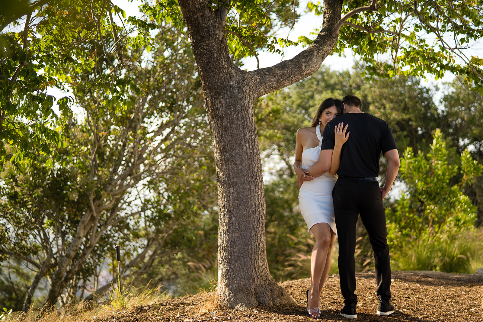 ThomasKim_photography A man and woman having a V & J Engagement Session under a tree, embracing in a hug.