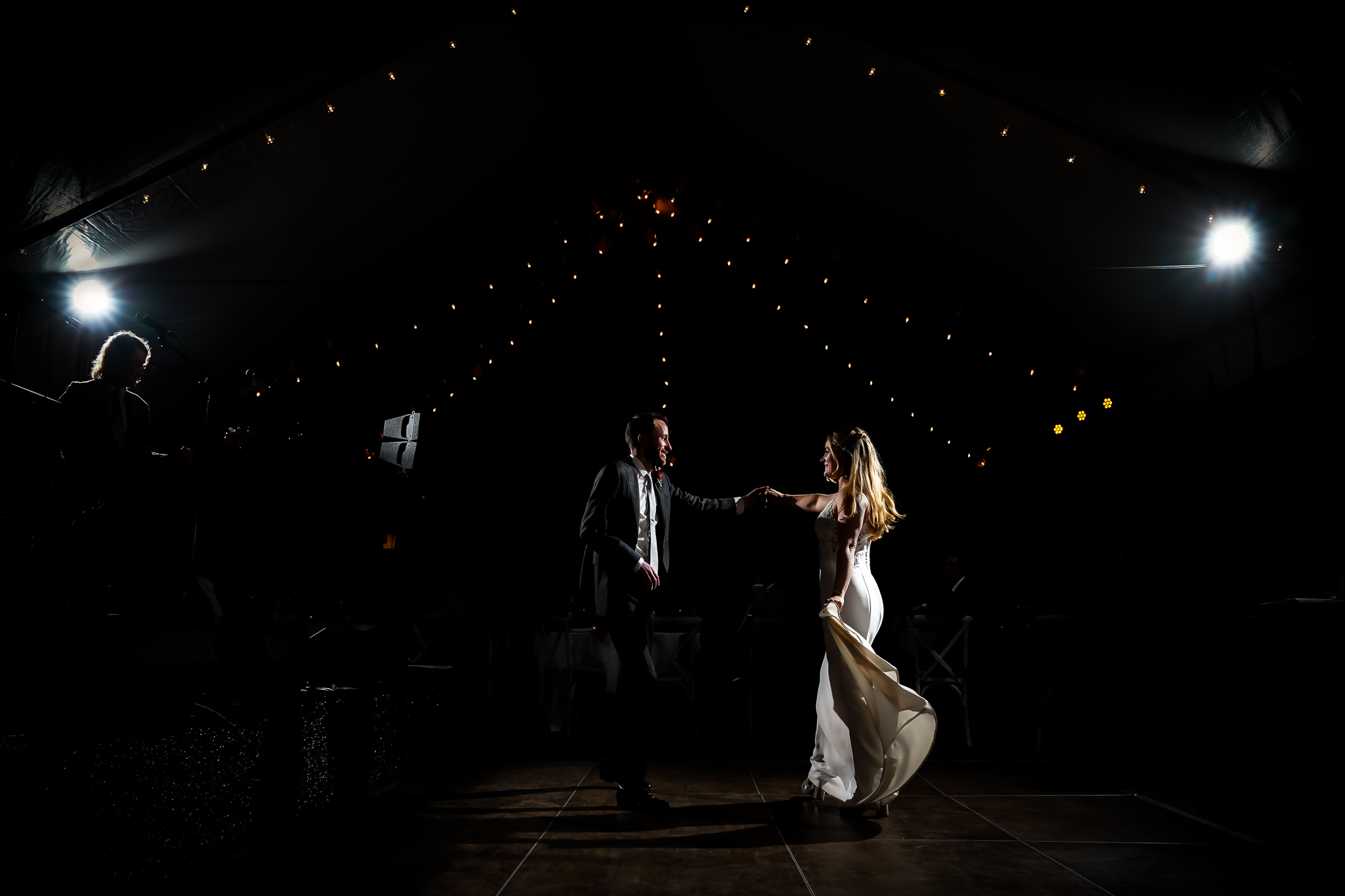 ThomasKim_photography A professional wedding photographer capturing a bride and groom dancing under a tent in the dark.